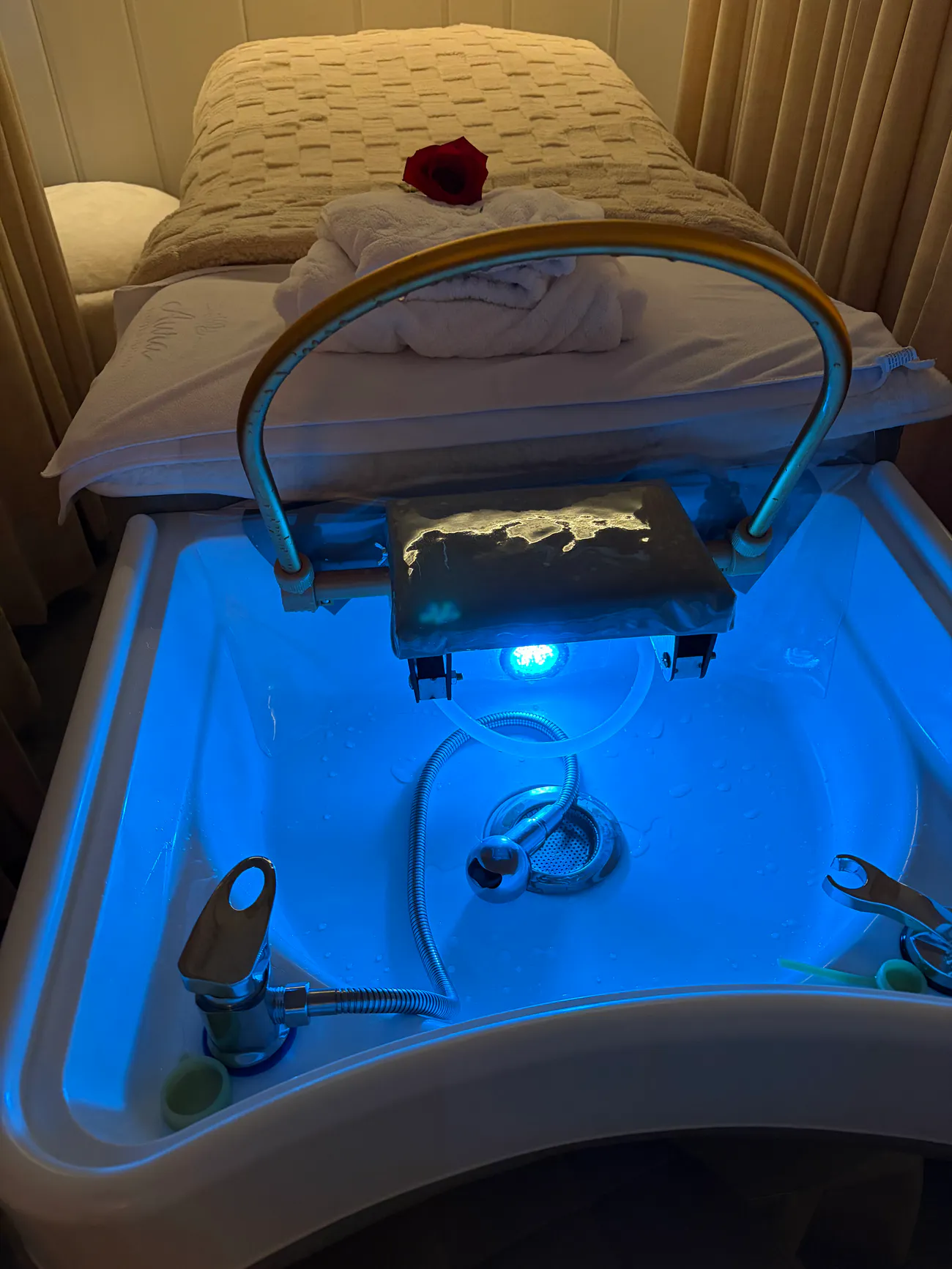The head spa basin at Aura, a shallow bowl lit blue from inside, with the gold rinse ring and its hose mounted on the arm above it