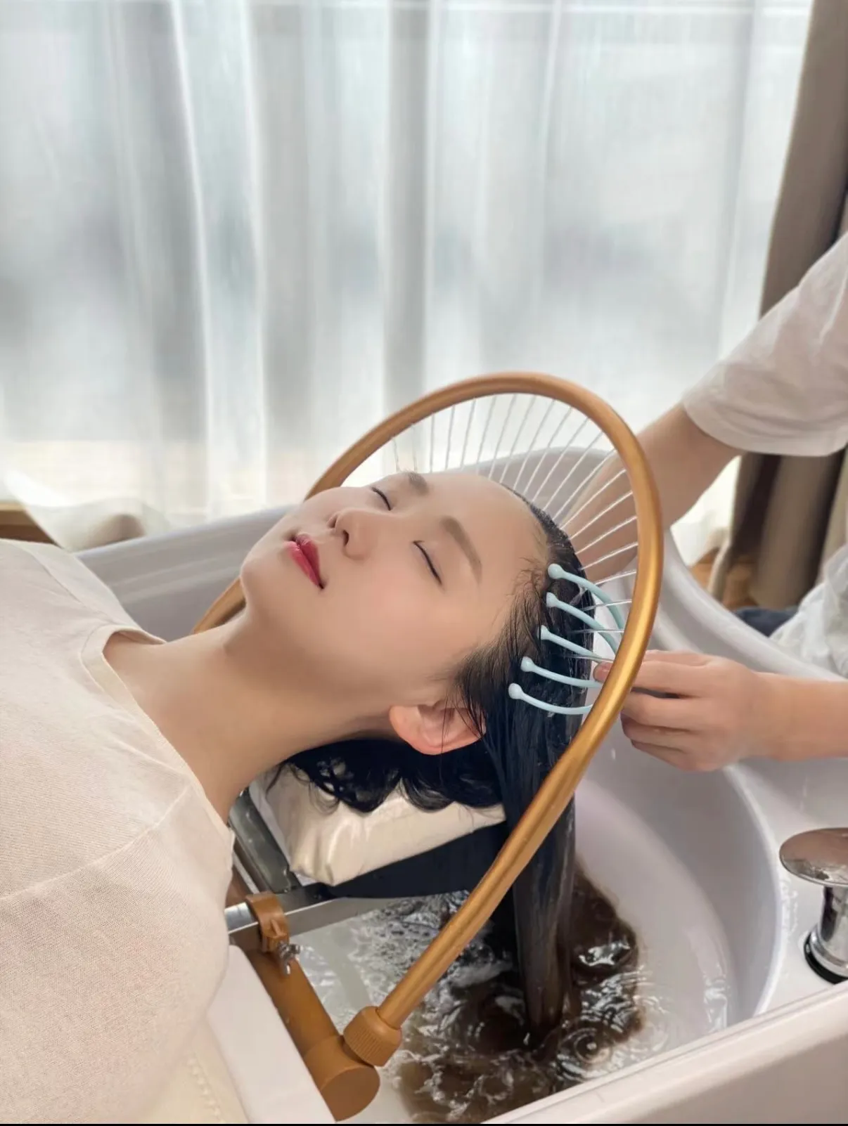 A guest lying back at Aura in Issaquah with her hair fanned out beneath the gold ring above the basin while warm water runs through it