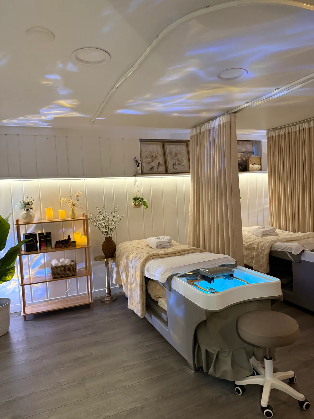 A treatment bed and basin at Aura in Issaquah behind a cream curtain divider, with rippling water-light on the ceiling